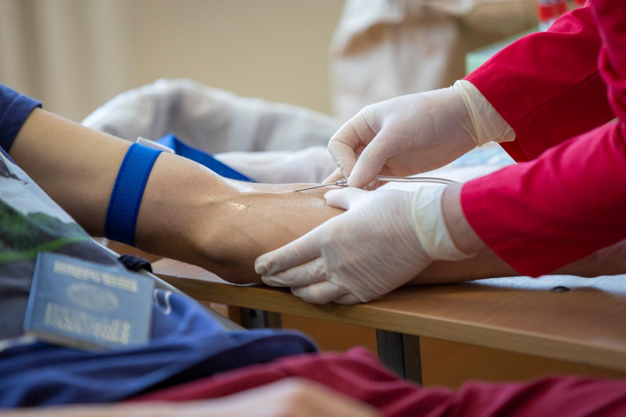 Medical professional drawing blood from donors arm in a clinical setting.